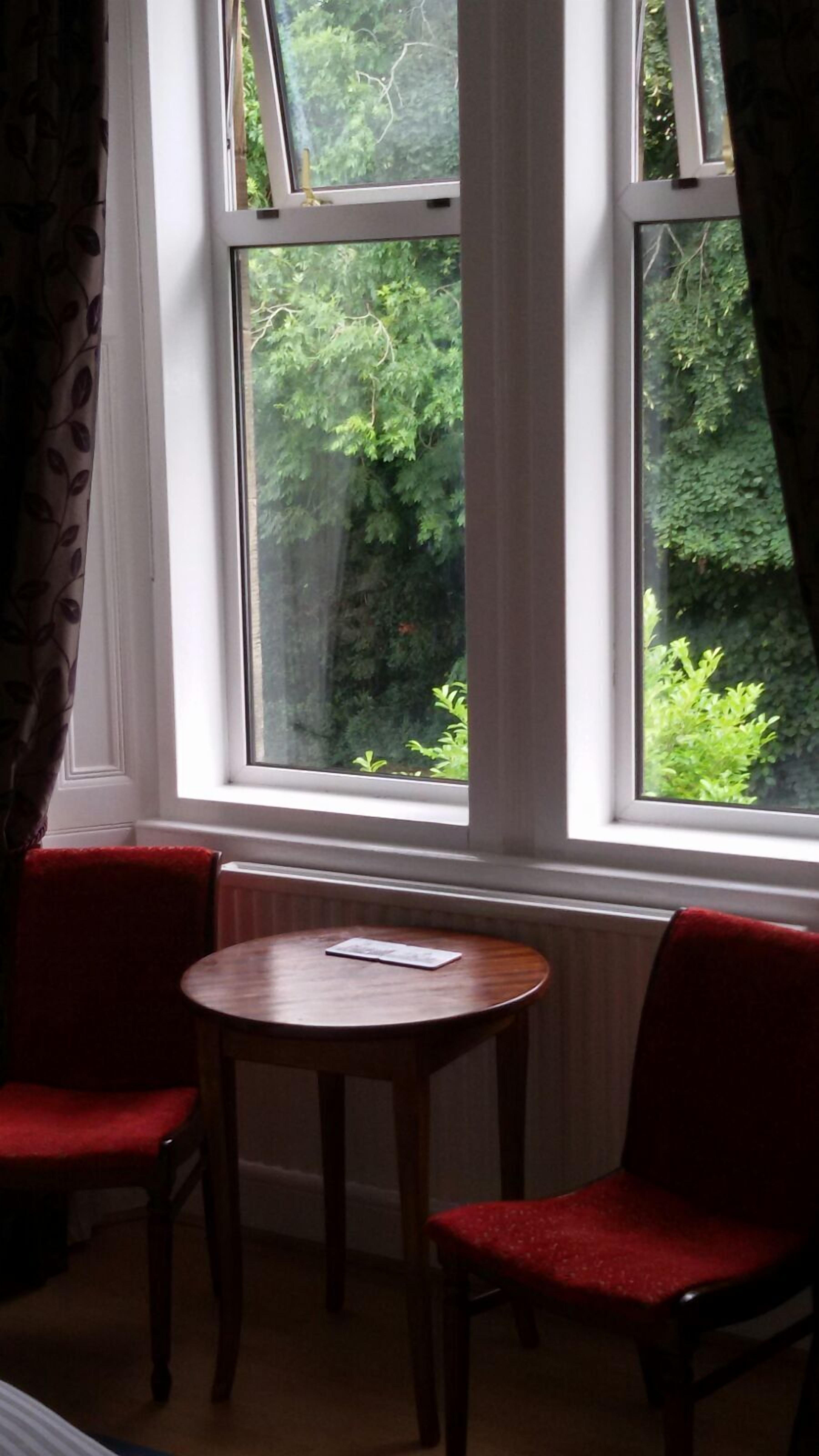 A room with a window overlooking greenery, a small round table, and two red chairs.