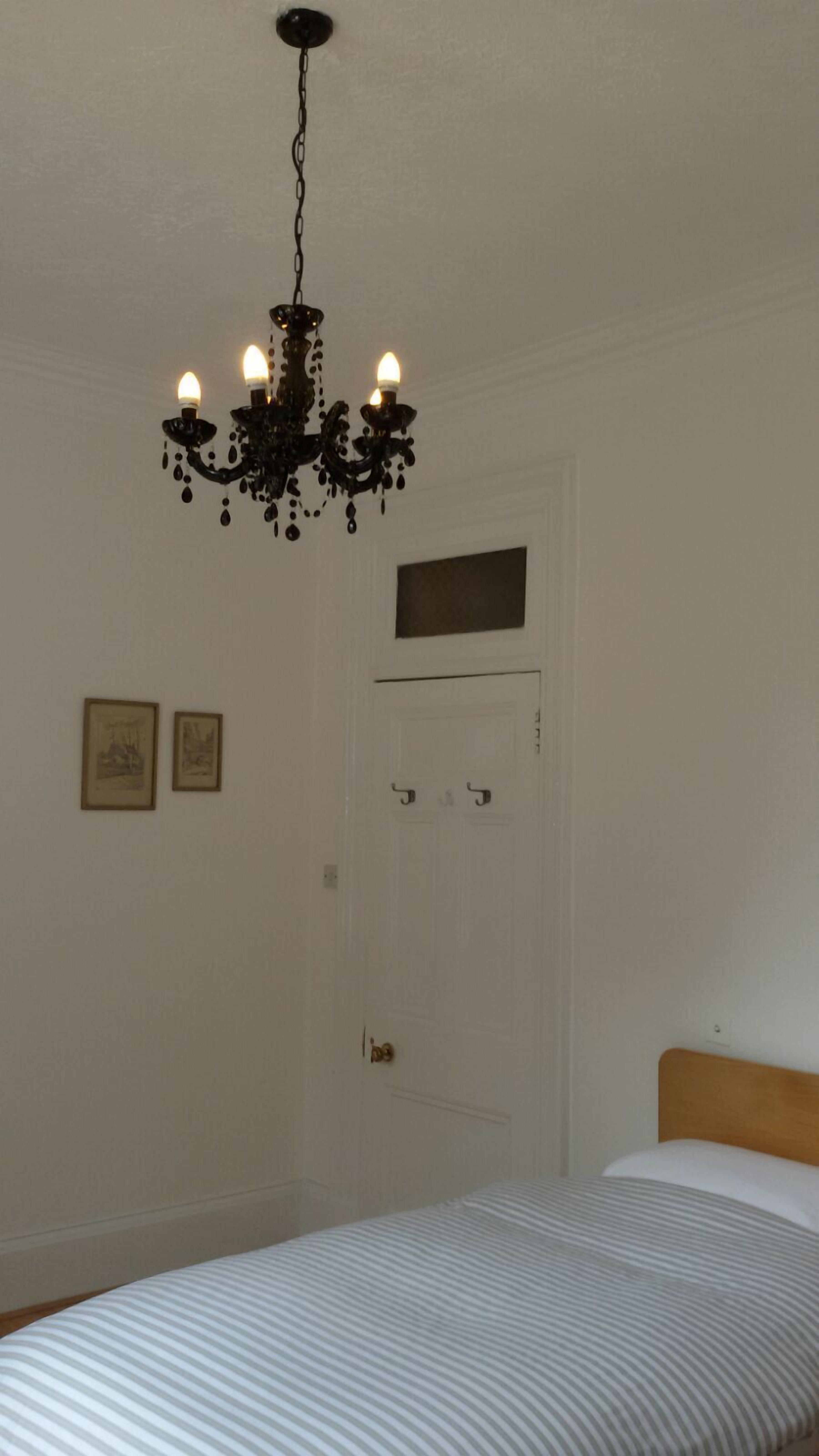 A bedroom with a bed, a white door, and a chandelier.
