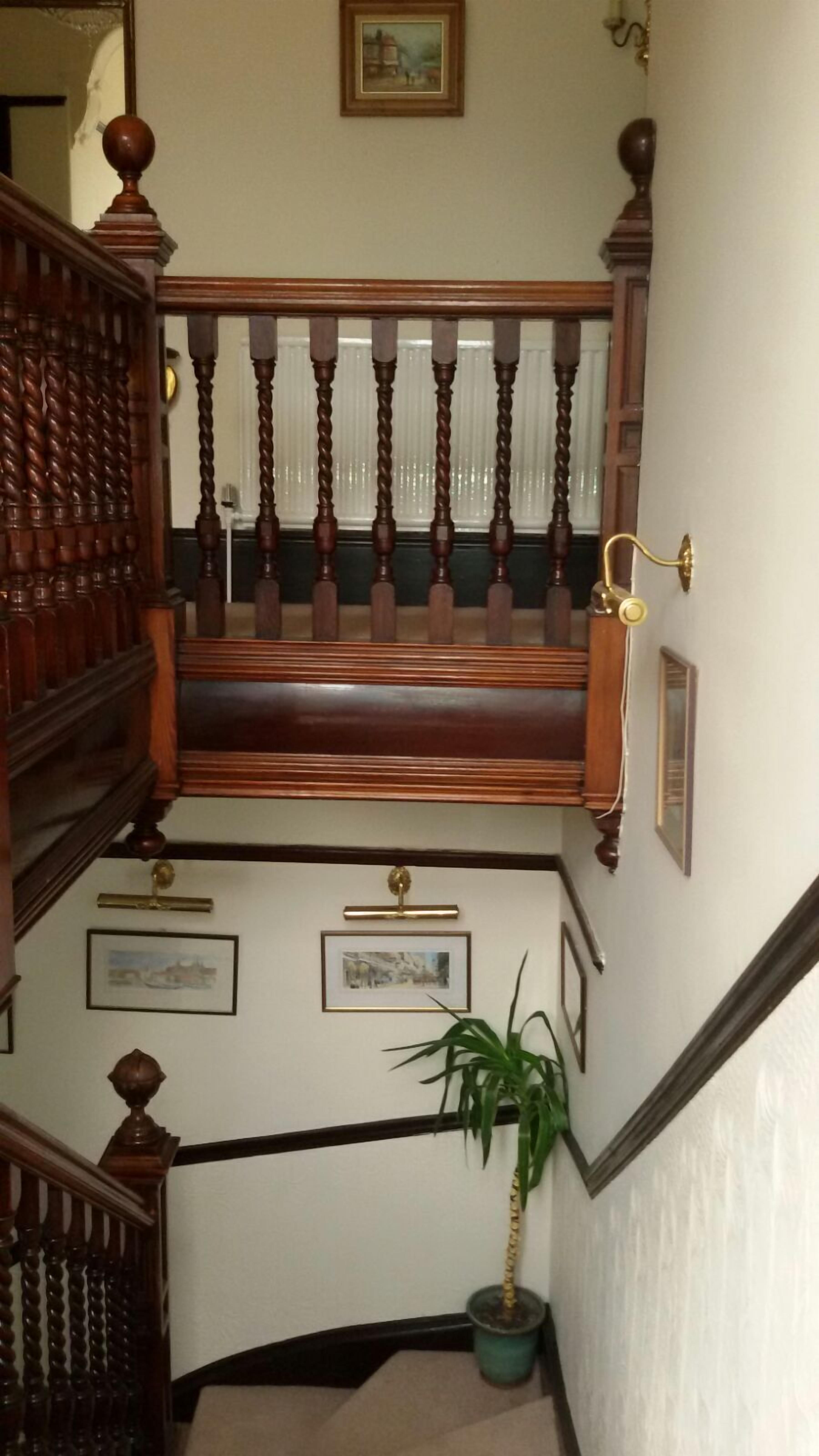 Una escalera con barandilla de madera, un banco y cuadros en las paredes.