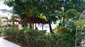 A lush garden with a thatched-roof structure, various plants, and a concrete pathway. - Lipe Village Resort (Koh Lipe)