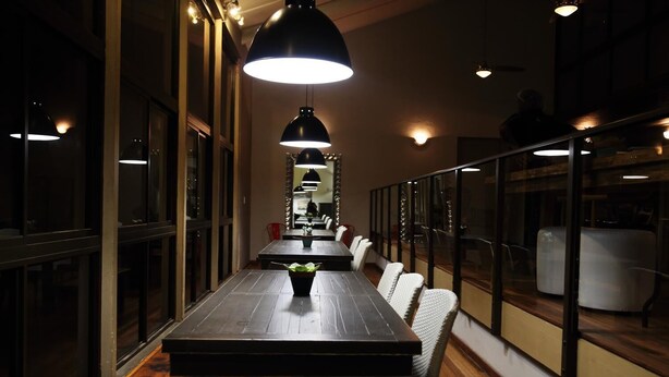 A long wooden dining table with a potted plant in the center, surrounded by white chairs. - The Backpack Shack - Hostel (Mossel Bay)