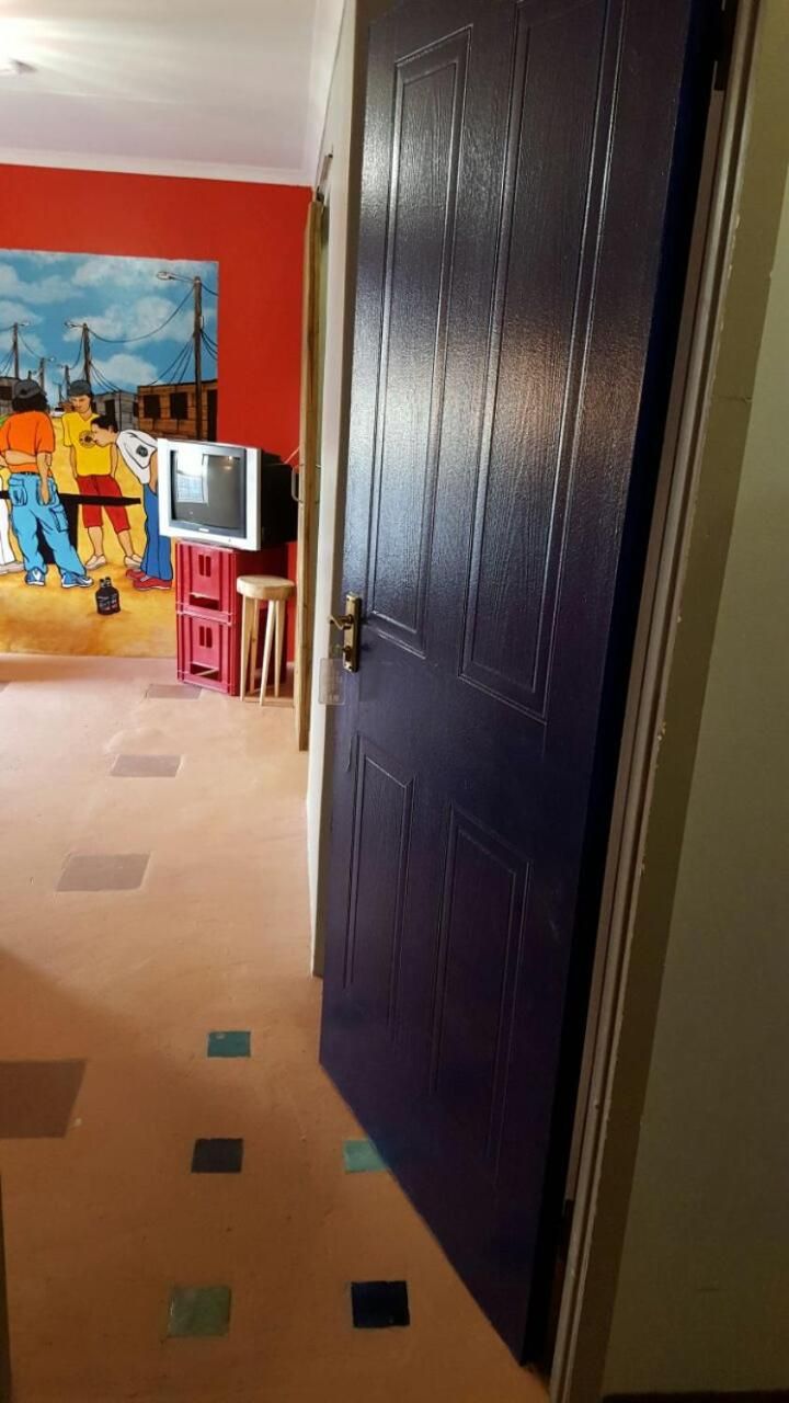 A hallway with a dark blue door, a red wall with a mural, and a small TV on a stand.
