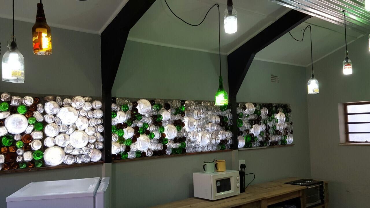 A room with a wall decorated with bottle caps, a microwave on a wooden table, and hanging pendant lights.