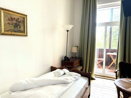 Un dormitorio con cama, mesita de noche con lámpara, un cuadro en la pared y vistas al exterior a través de una ventana.