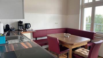 Cocina compacta con estufa integrada, lavamanos y comedor con mesa y sillas tapizadas en rojo.