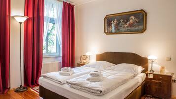 Una habitación de hotel con una cama doble, dos mesitas de noche con lámparas, un cuadro en la pared y una ventana con cortinas rojas.