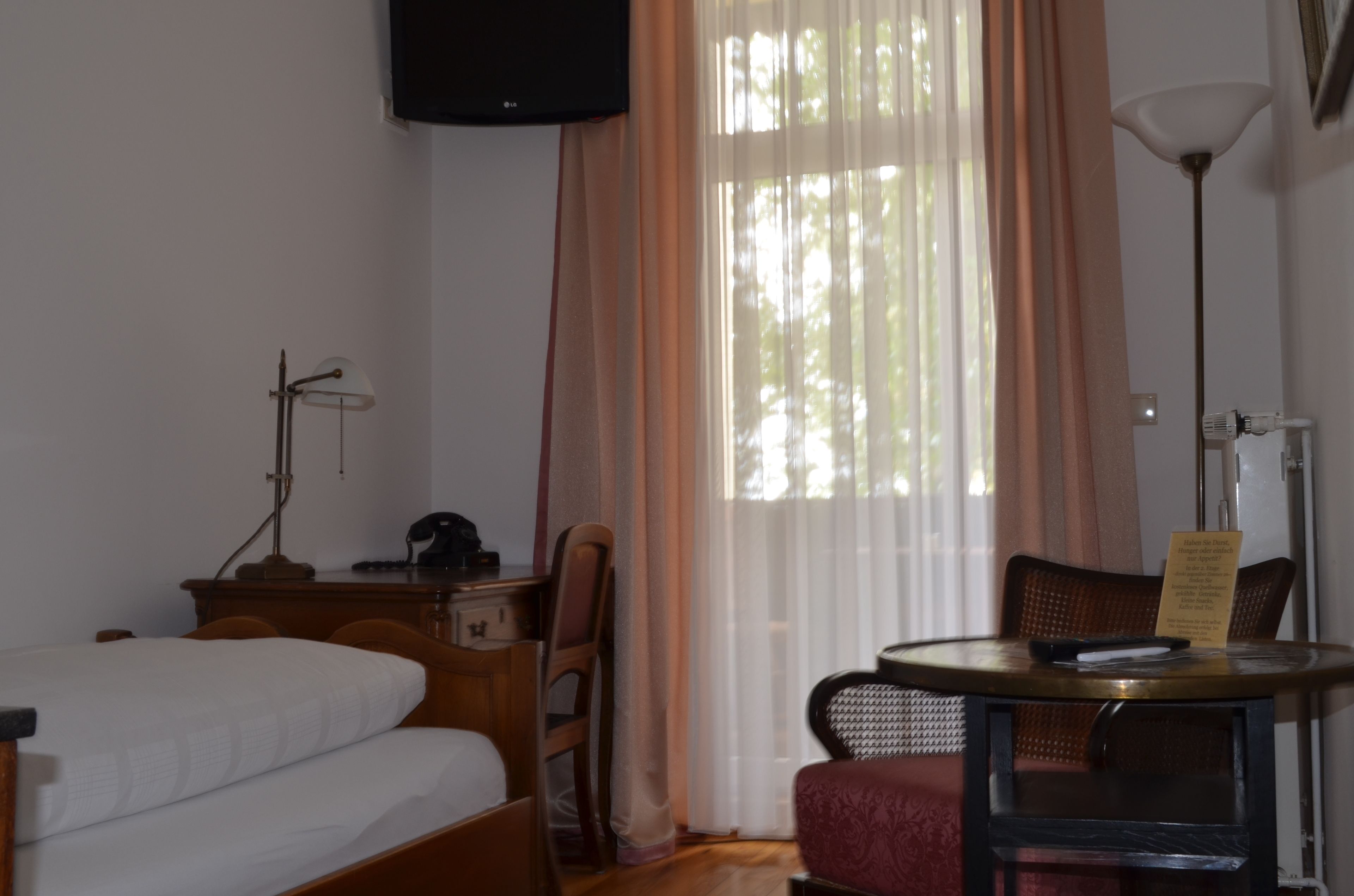 A hotel room with a bed, a desk, a chair, a table, and a TV mounted on the wall.