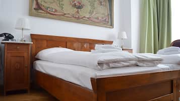 A neatly made bed with white linens, a wooden headboard, a nightstand with a lamp, and a painting on the wall.