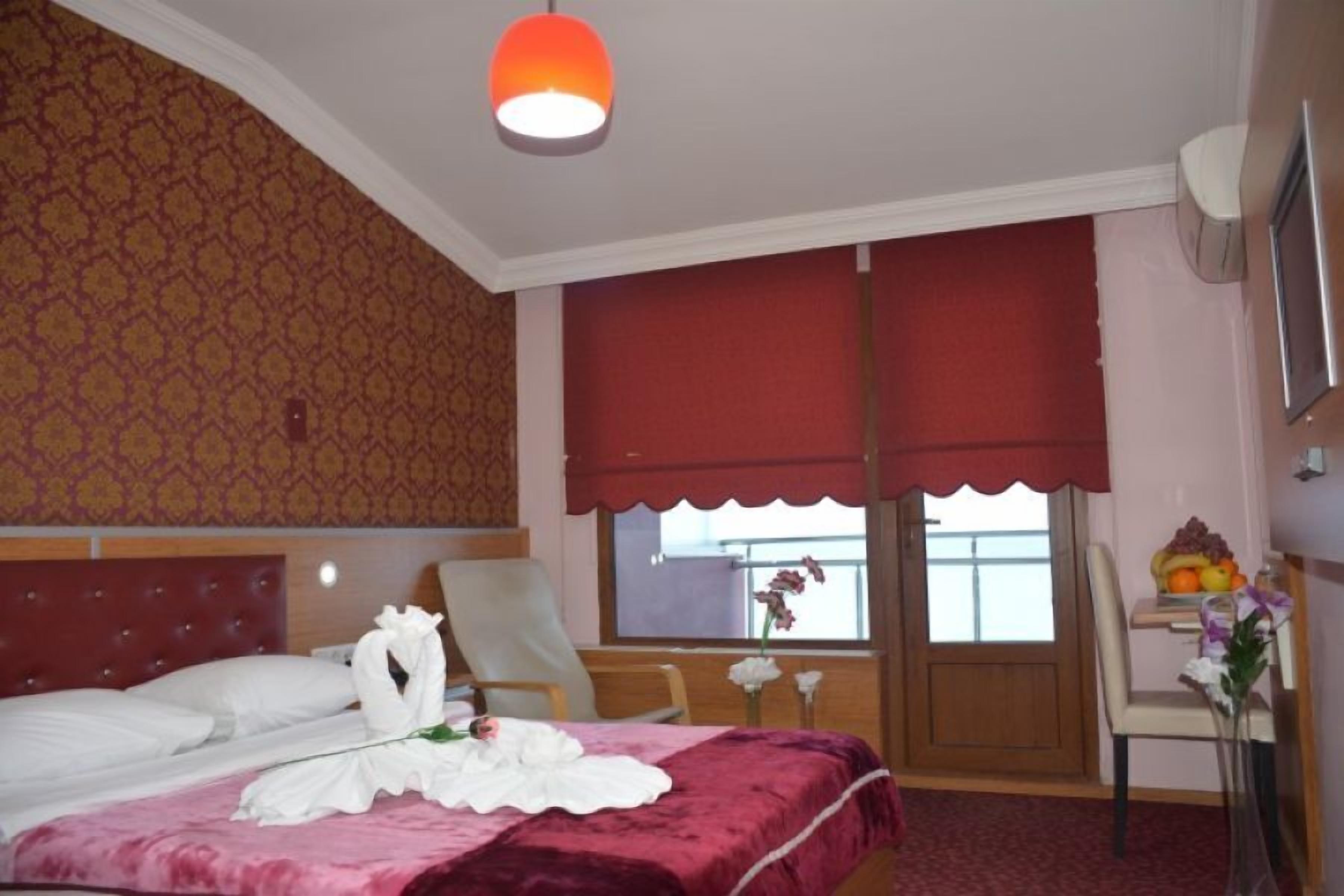A hotel room with a bed, a chair, a table with fruit, and a window with a view.