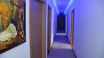 Un pasillo con techo iluminado en azul, un cuadro en la pared izquierda y puertas que dan a habitaciones.