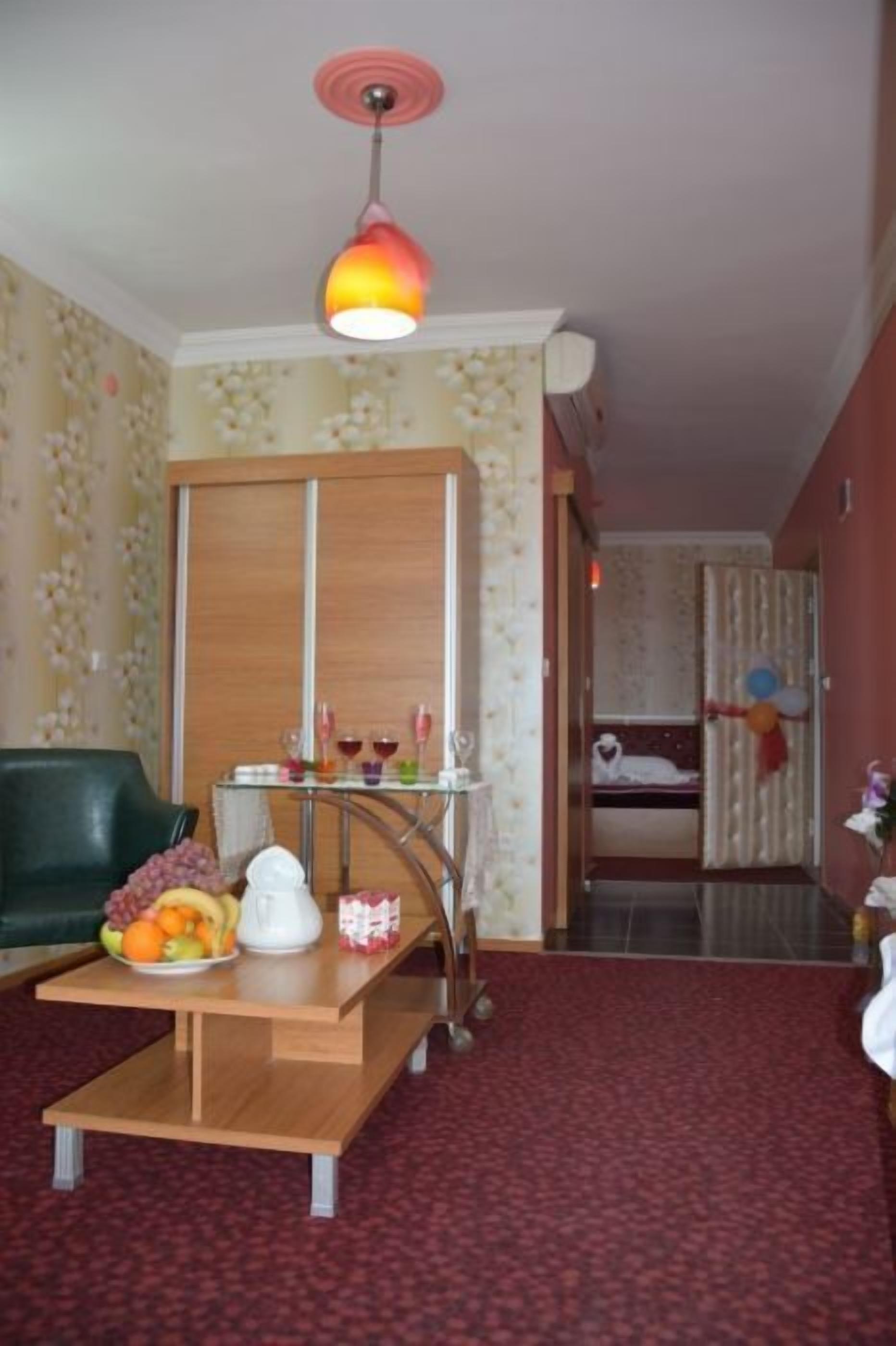 Una habitación con una mesa de madera, un sofá verde, un carrito pequeño con una tetera blanca y una cama con cortina a rayas.