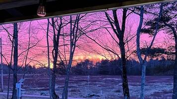 Näkymä auringonlaskusta paljaiden puiden läpi, ja etualalla näkyy puinen rakennelma.