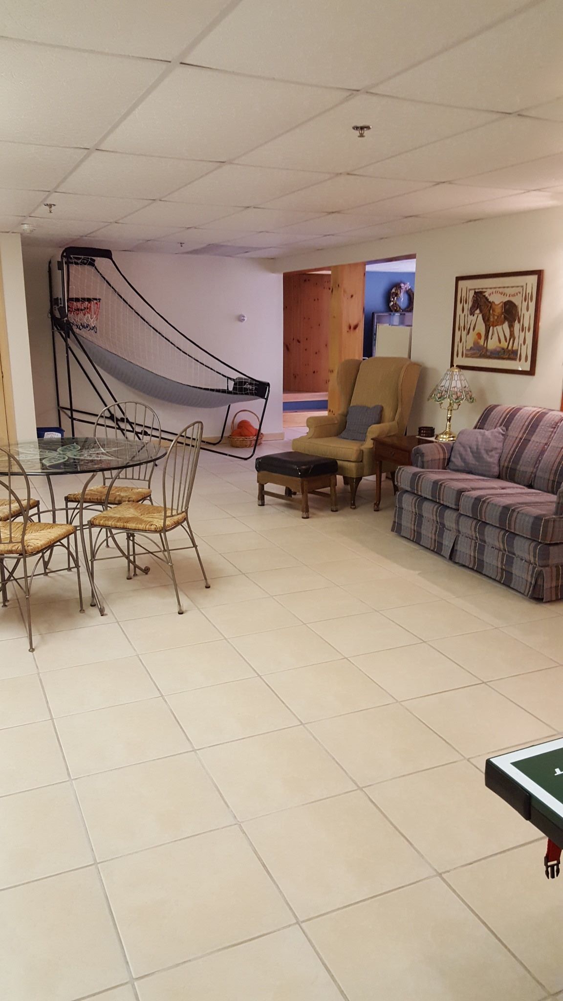 Un salon comprenant une table à manger avec un plateau en verre, des chaises en osier, un canapé et un fauteuil.