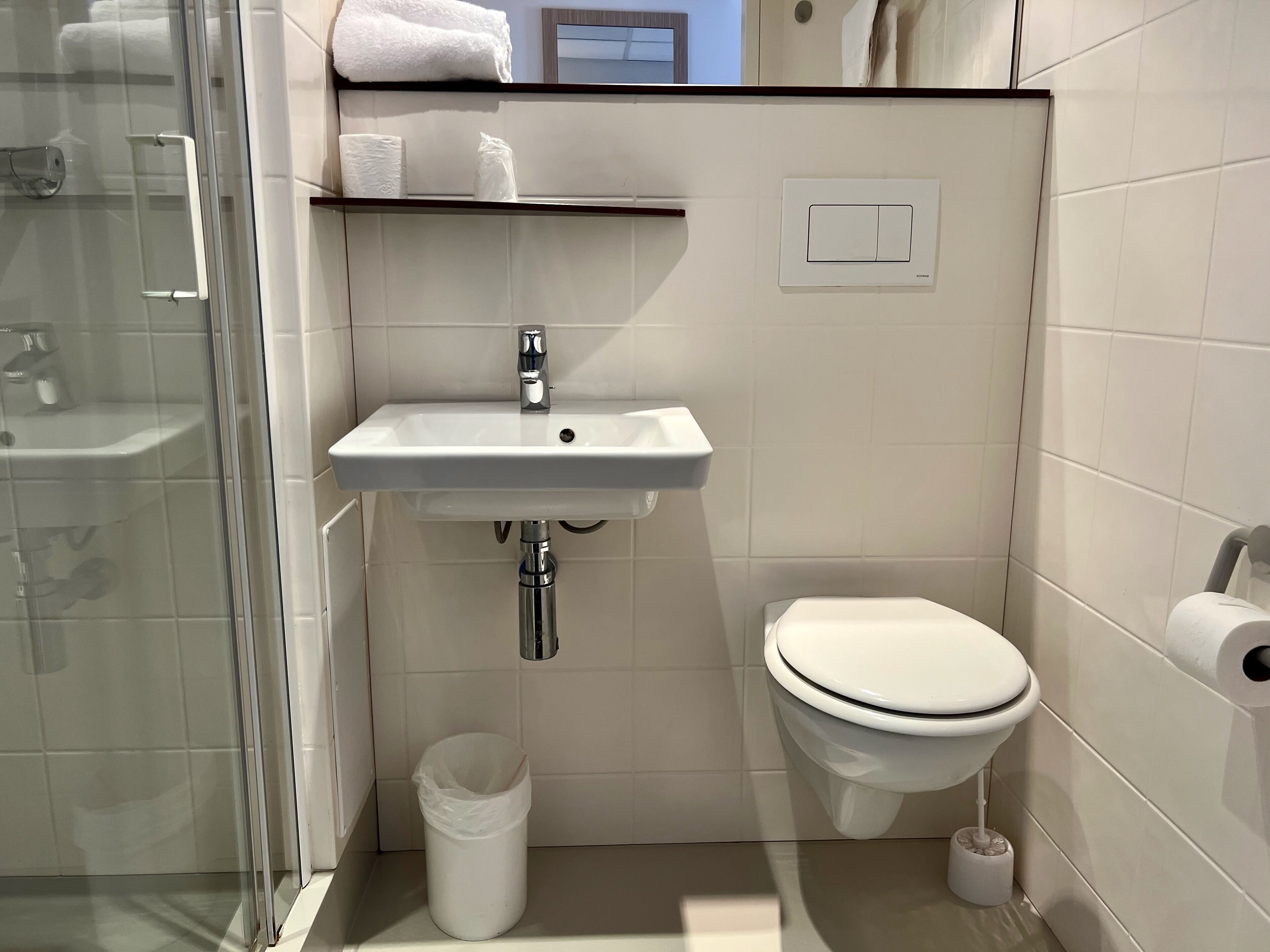 Une petite salle de bain avec un lavabo blanc, des toilettes et une douche à parois de verre.