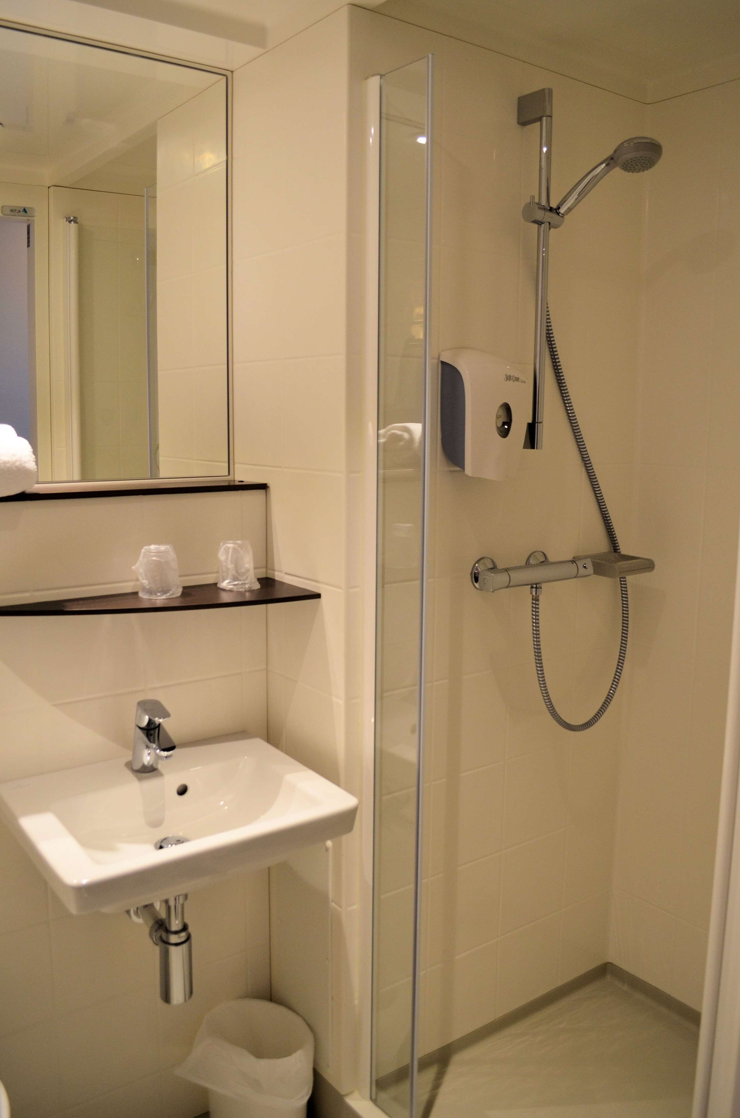 Un baño moderno con cabina de ducha de vidrio, un lavabo con espejo y un pequeño cubo de basura.