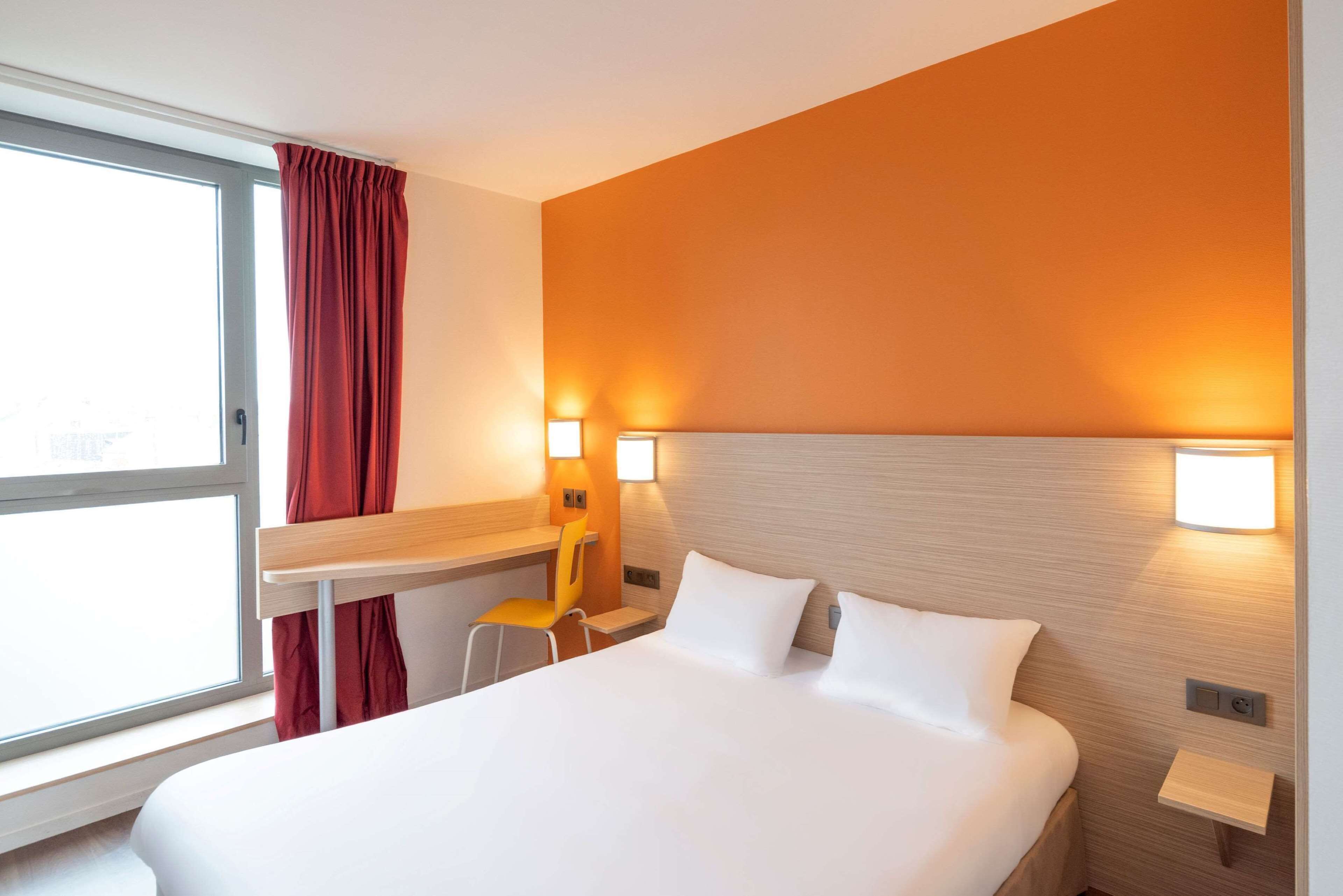 A hotel room with a bed, a desk, a chair, and two wall-mounted lights.