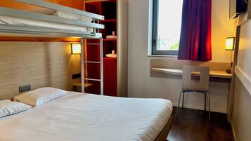 Una camera d'albergo con un letto a castello, una scrivania con sedia, un armadio e una finestra con tende.