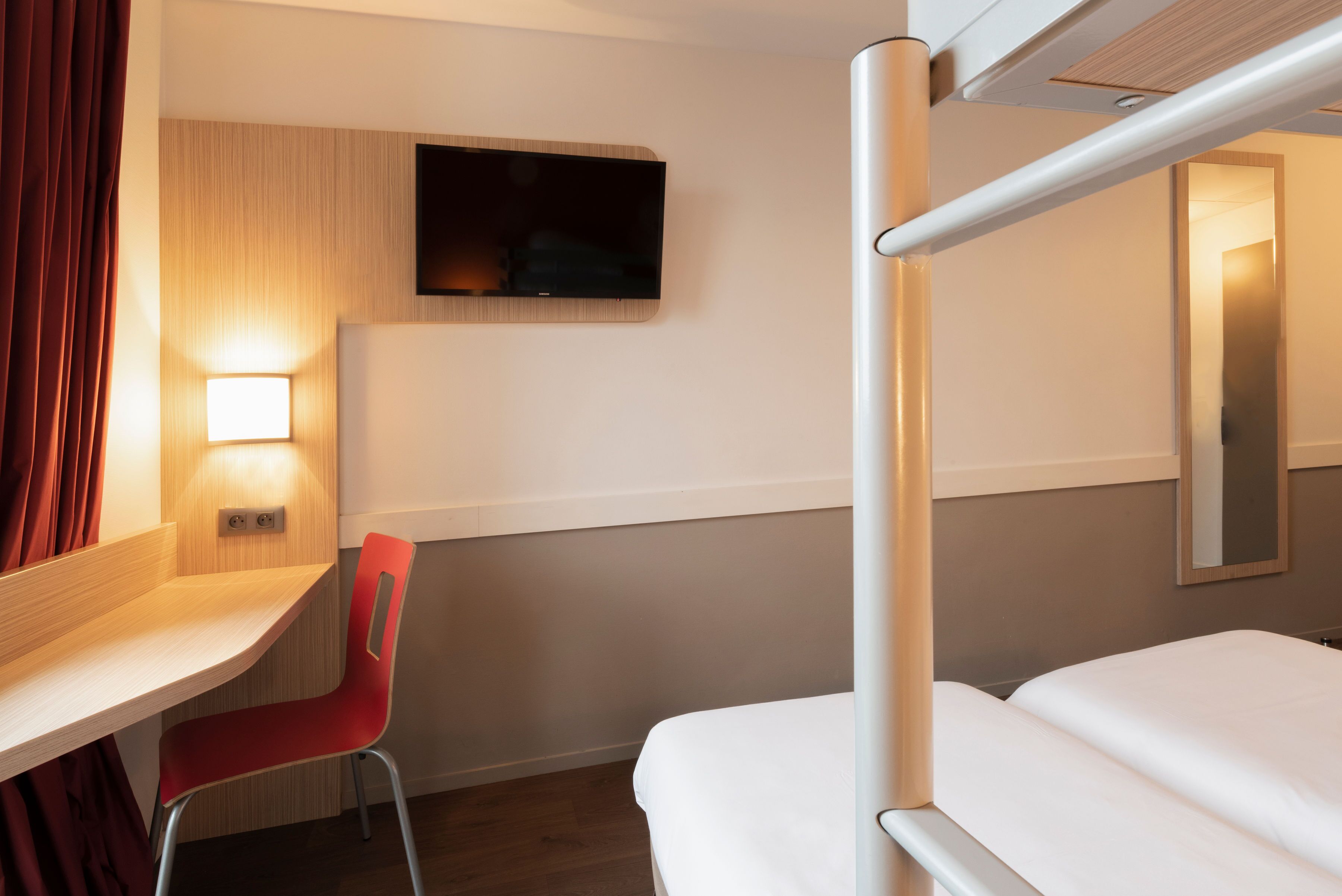 Ein Hotelzimmer mit Etagenbett, Schreibtisch mit Stuhl, flachbildschirmfernseher an der Wand und Nachttisch mit Lampe.