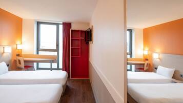 Une chambre d’hôtel avec deux lits, un bureau, une chaise, un téléviseur fixé au mur et une fenêtre avec des rideaux.