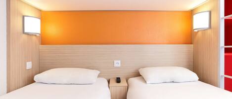 A hotel room with two beds, wooden headboard, orange accent wall, bedside lamps, and a red closet.