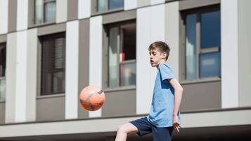 Un niño juega con una pelota de fútbol frente a un edificio moderno.