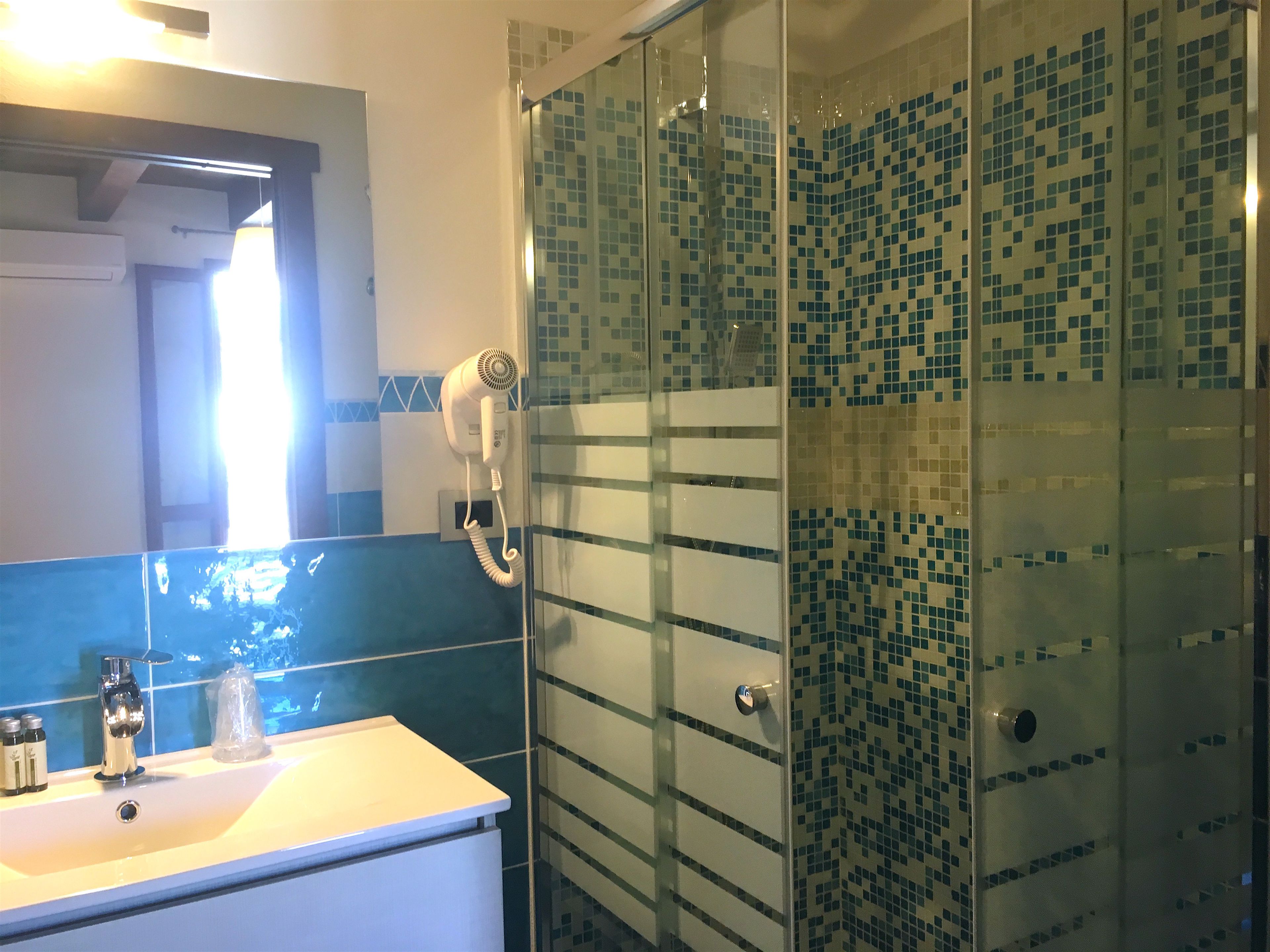 Een badkamer met een douchecabine van glas, een wit wastafelmeubel en een blauwe betegelde spatwand.