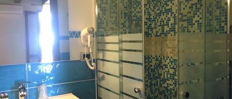 A bathroom with a glass shower enclosure, a white sink with a mirror above it, and a blue tiled backsplash.