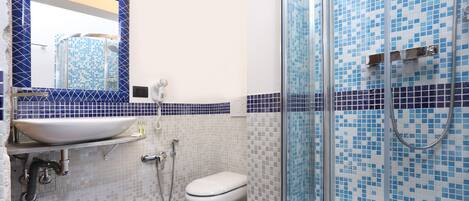 Un baño con lavamanos blanco, inodoro y ducha con mosaicos azules.