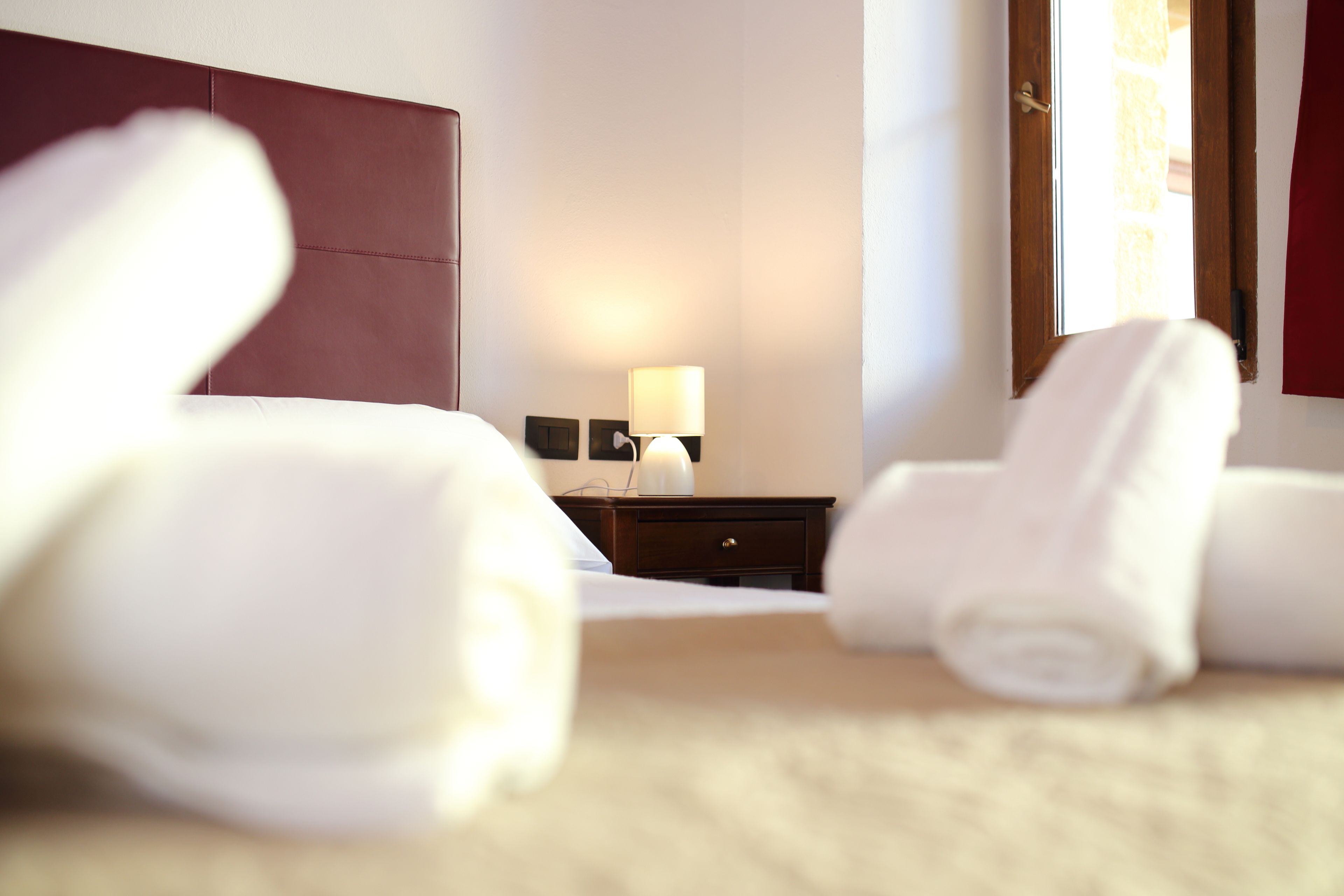 Habitación de hotel con cama, mesita de noche con lámpara y toallas enrolladas en el suelo.