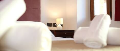Habitación de hotel con cama, mesita de noche con lámpara y toallas enrolladas en el suelo.