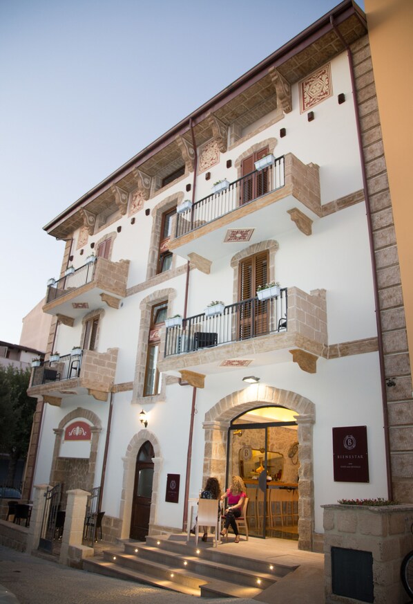 A building with a stone facade, multiple balconies, and a bar area with a sign. - Bienestar  Maison de Charme (Alghero)