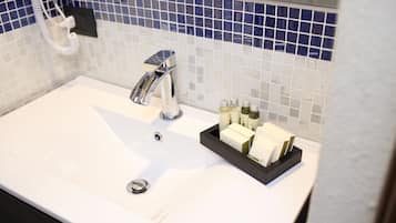 Et badeværelsesvask med kromarmatur, et spejl og en bakke med toiletartikler.