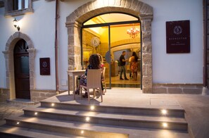 Entrada de restaurante com arco de pedra, um candelabro e uma placa com a inscrição 'Bienestar Food and Beverage'.