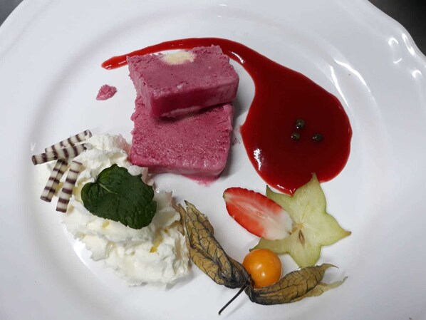 A dessert plate with pink mousse, whipped cream, strawberries, a cherry, and a decorative leaf. - Harmonie Stüberl (Ottnang am Hausruck)