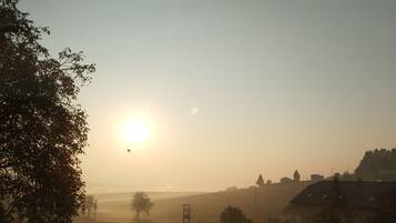 A rural landscape with a clear sky, a sun low on the horizon, and a few scattered buildings.