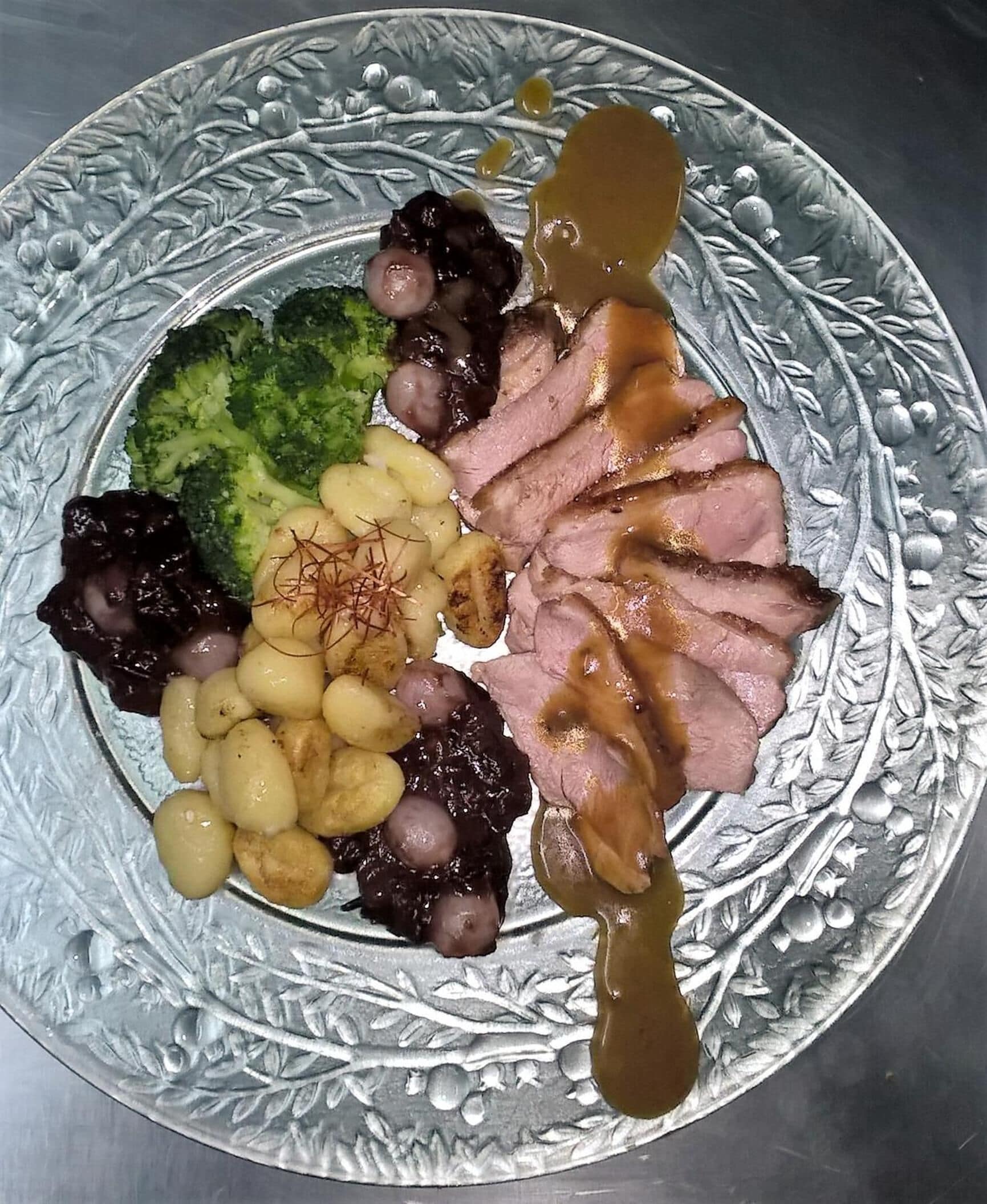 A plate with sliced meat, broccoli, and beans, accompanied by a sauce.