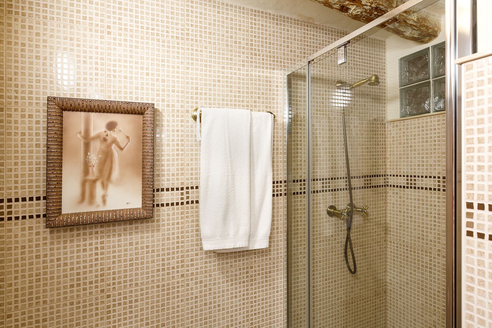 A bathroom with mosaic tile walls, a framed picture, and a shower with a glass door.