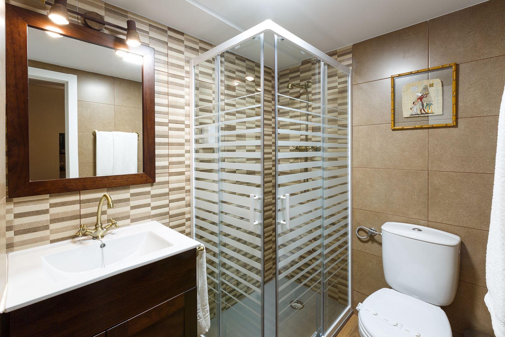 A bathroom with a glass shower enclosure, a white sink with a gold faucet, and a toilet.