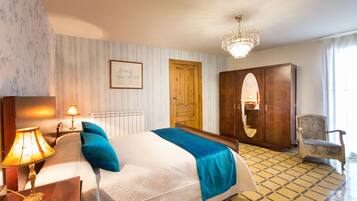 A hotel room with a bed, a wooden wardrobe, a chair, a lamp, and a picture on the wall.