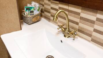 A bathroom sink with a gold faucet, a drain, and a basket of toiletries on the counter.
