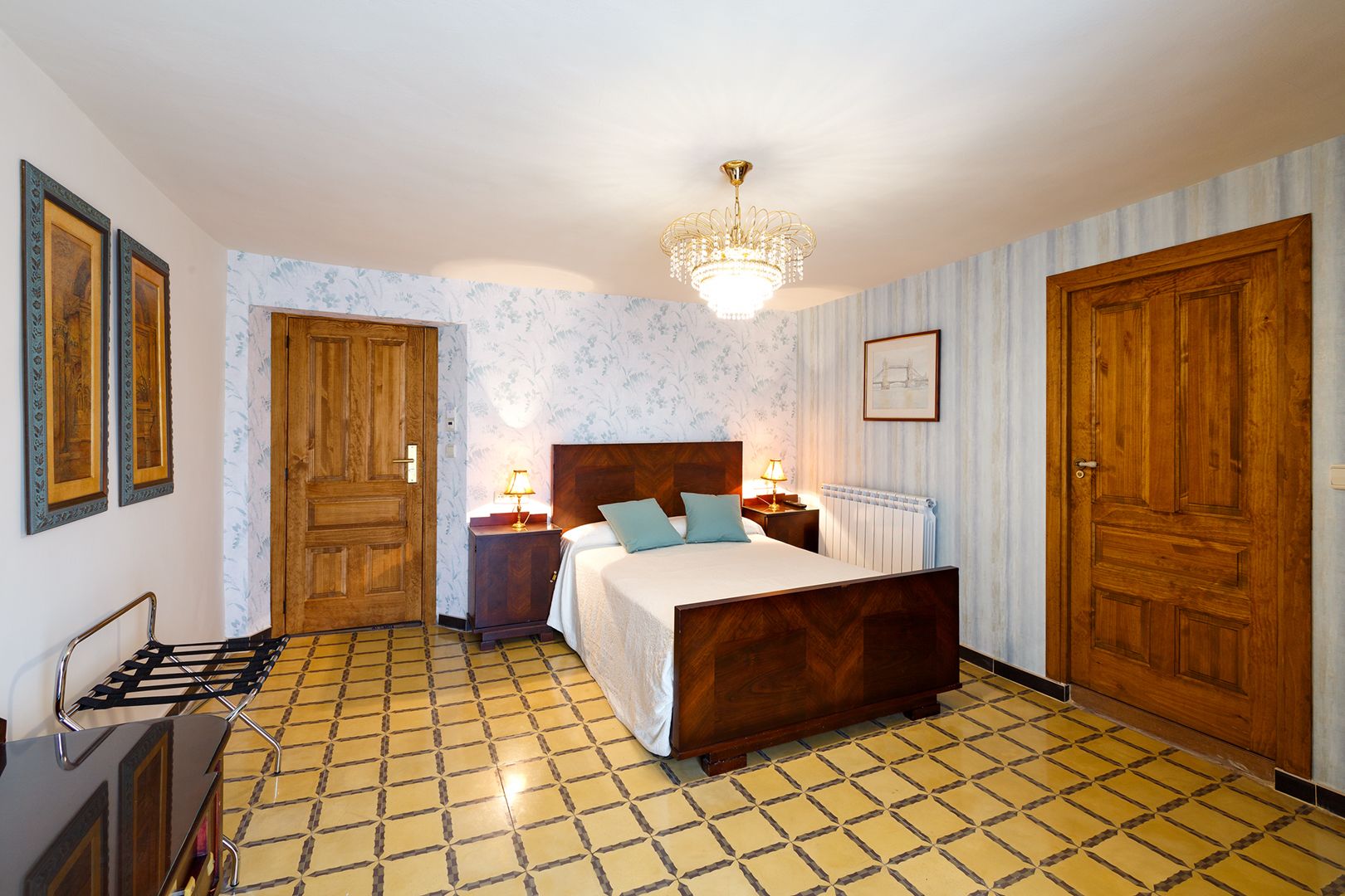 A bedroom with a wooden bed, two bedside tables with lamps, a radiator, and a chandelier.