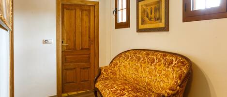 Una habitación con puerta de madera, un sofá estampado y dos cuadros en la pared.