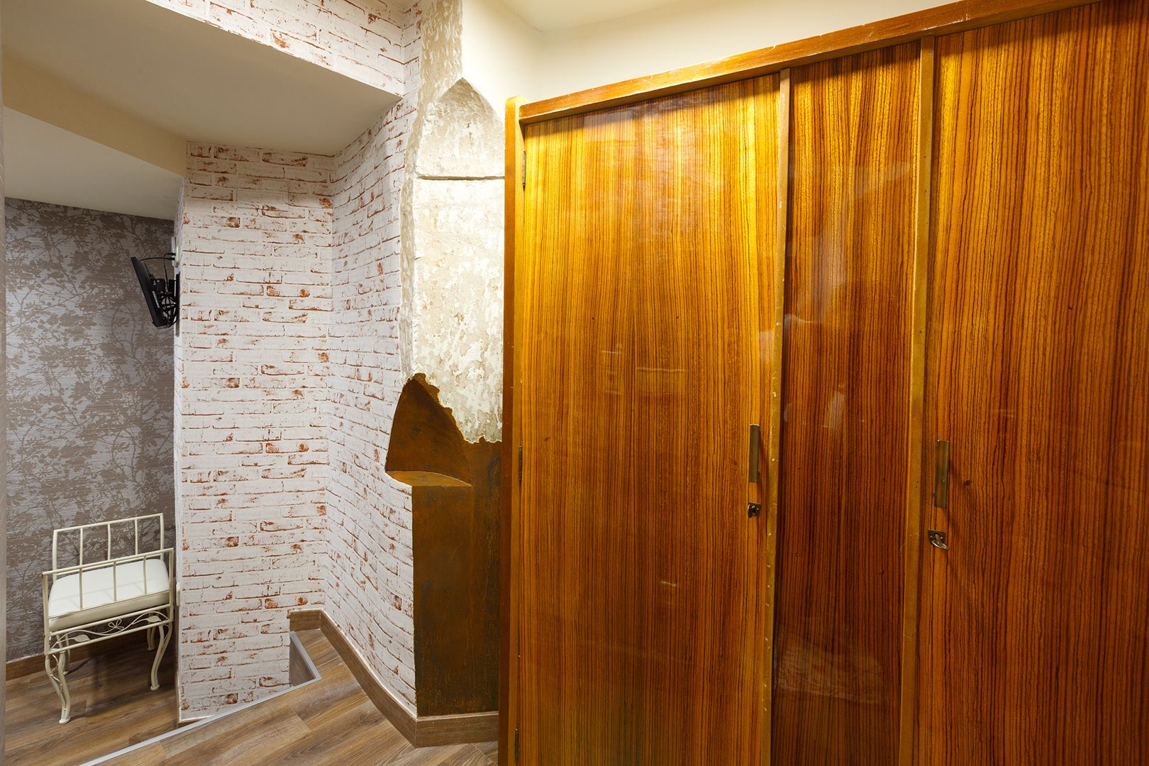 Una habitación con un armario de madera, una pared de ladrillo blanco y una estructura de cama metálica.