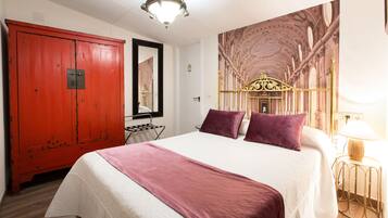 A hotel room with a large bed, a red wardrobe, a chandelier, and a wall mural.