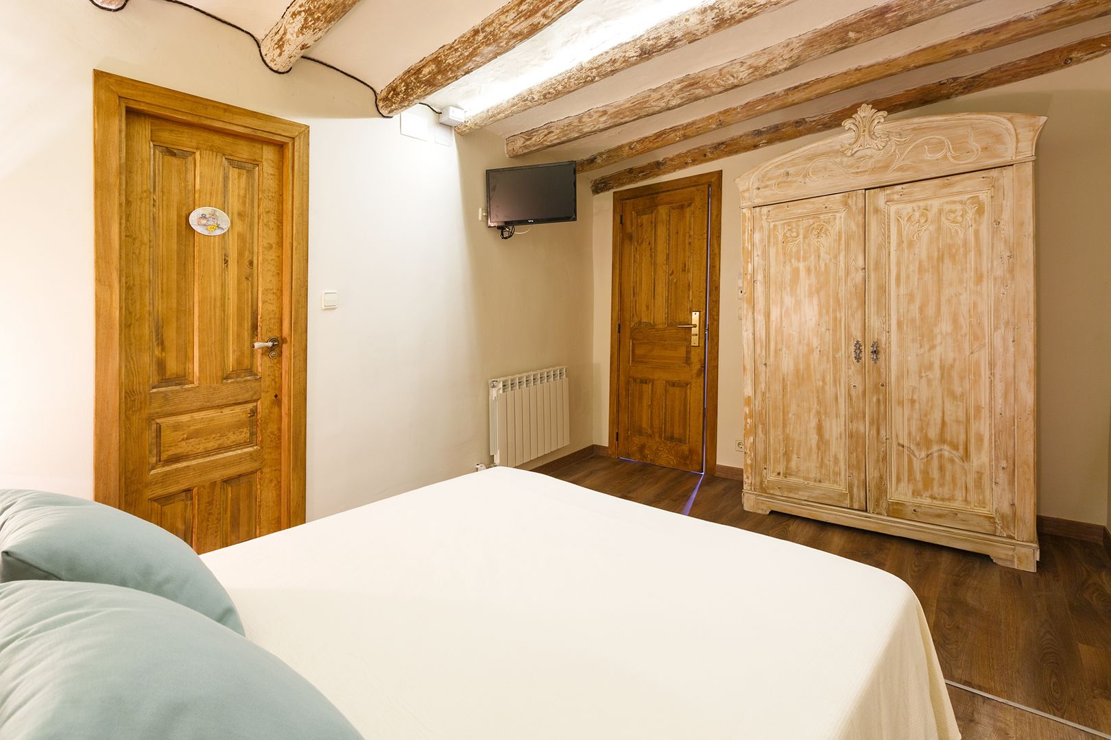 Une chambre à coucher avec un lit, une armoire en bois et un téléviseur fixé au mur.