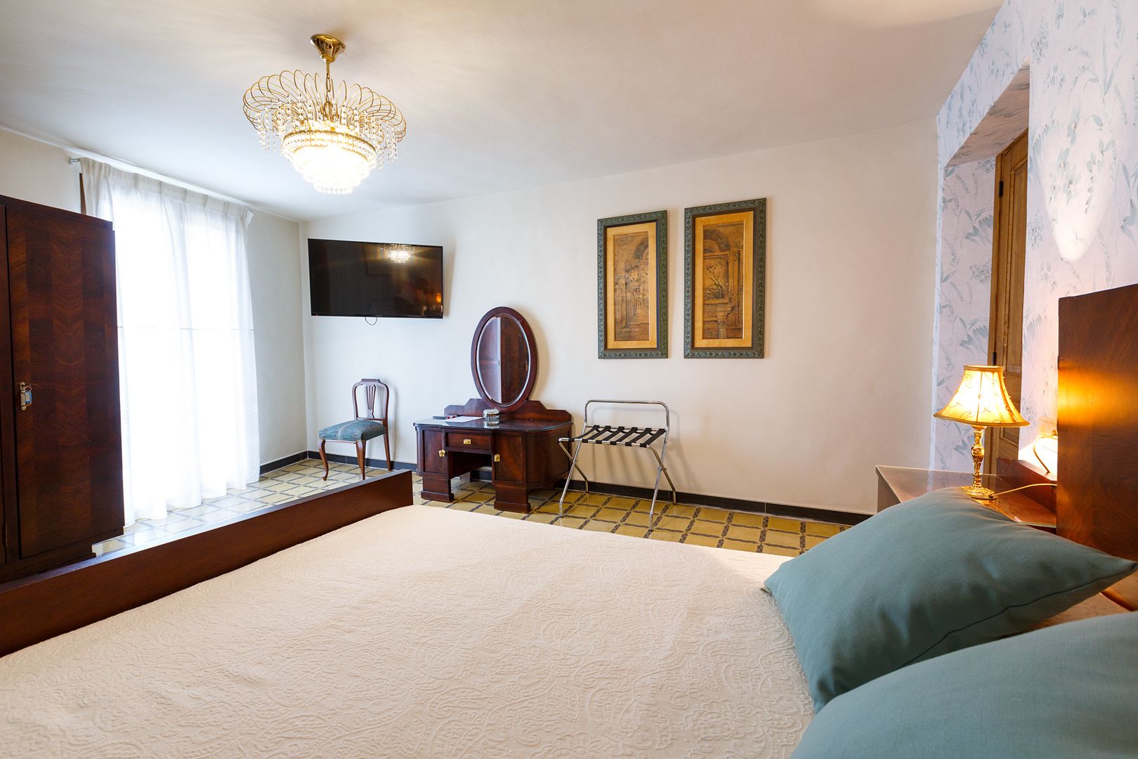 Un dormitorio con una cama grande, un aparador, una cómoda con espejo, un televisor montado en la pared y dos cuadros enmarcados.