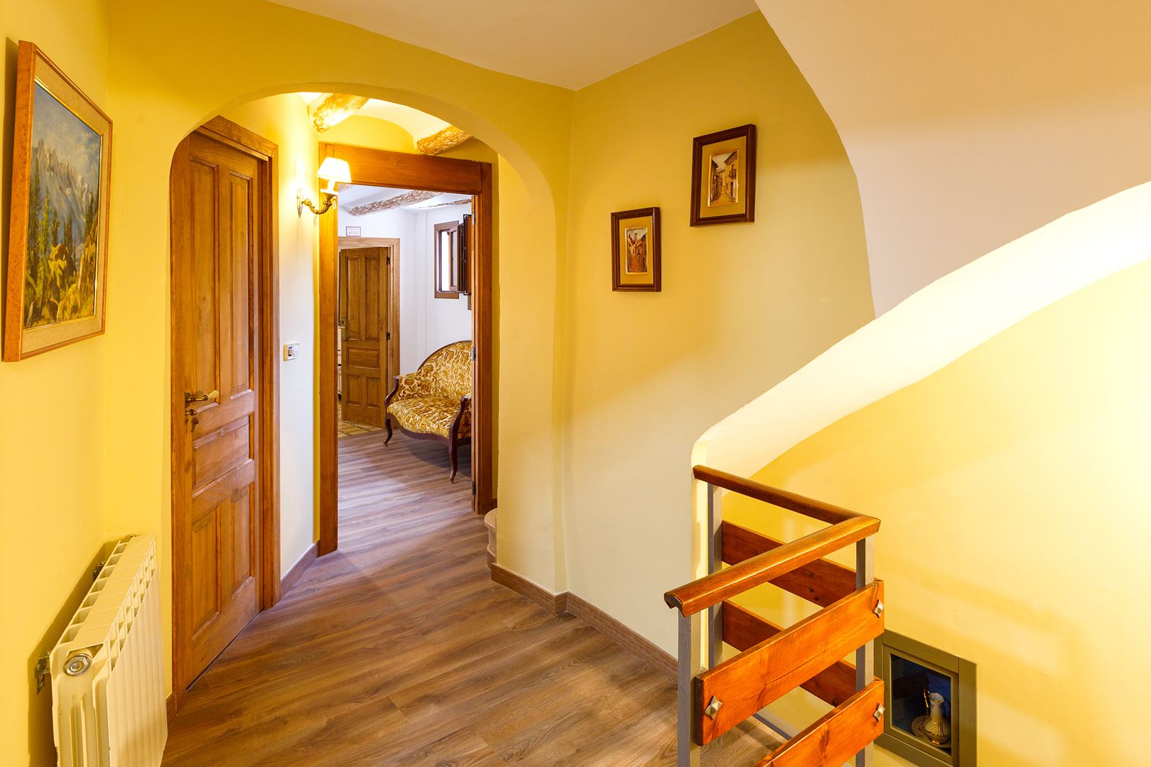 A hallway with wooden flooring, a staircase with a wooden handrail, and a radiator on the left.