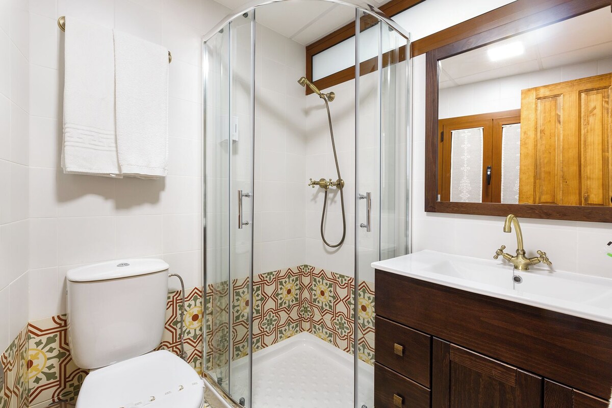 Une salle de bain avec une douche à parois de verre, des toilettes blanches, une baignoire et un meuble-lavabo en bois avec un miroir.