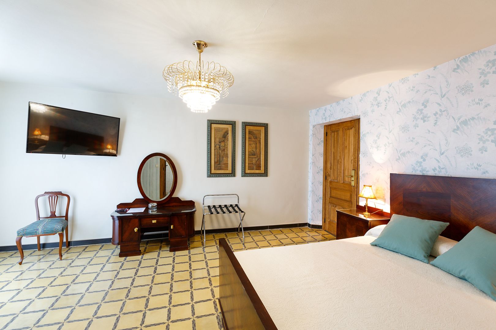 Habitación de hotel con una cama, cómoda de madera, una silla, un espejo, televisor y dos cuadros en la pared.