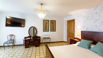 Habitación de hotel con una cama, cómoda de madera, una silla, un espejo, televisor y dos cuadros en la pared.